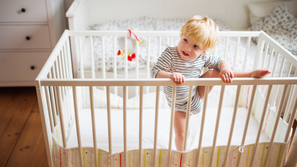 A child too big for his crib, and is trying to climb out with his leg over the crib. Displaying signs of climbing out