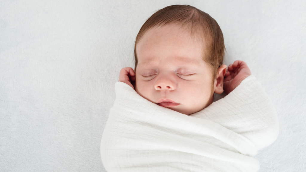 A baby sleeping swaddled and displaying a Firm Sleep Surface: covered by a fitted sheet.